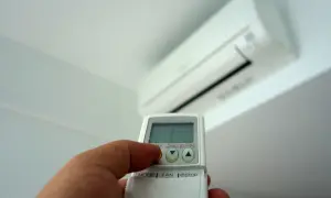 Mano con mando a distancia ajustando el aire acondicionado. Averigua cuanto gasta un aire acondicionado por hora para ahorrar energía.