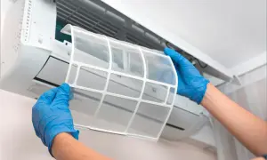 Manos con guantes azules retiran filtro de aire acondicionado. El mantenimiento es clave para saber cuanto dura un aire acondicionado.