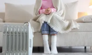 Persona abrigada con manta y calcetines sentada en sofá, junto a un radiador eléctrico. ¿Qué sistema de calefacción elegir para estar cómodo?