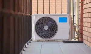 Unidad exterior de aire acondicionado, parte de una instalación de aire acondicionado exterior, en un balcón con barandilla y pared de ladrillo.
