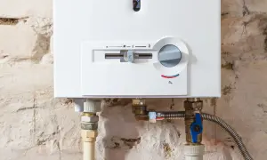 Detalle de una caldera mixta blanca con controles y tuberías conectadas a una pared de ladrillo.