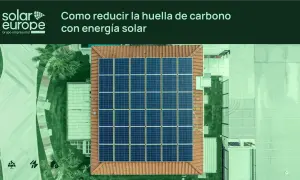 Vista aérea de un tejado con un gran conjunto de placas solares. El texto indica "Cómo reducir la huella de carbono con energía solar".