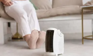 Persona sentada con calcetines gruesos, disfrutando del calor de un calefactor portátil, el mejor sistema de calefacción para un piso.