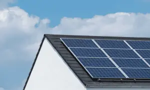 Paneles solares en tejado de casa blanca, bajo un cielo azul con nubes. ¿Cuántas placas solares necesito para una casa?