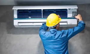 Técnico con casco amarillo ajusta un aire acondicionado, buscando reducir los decibelios del aire acondicionado para un ambiente más silencioso.