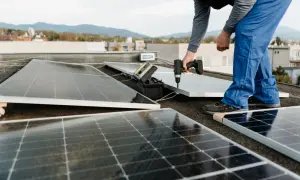 Instalación de un panel solar para aire acondicionado en una azotea. Un técnico usa un taladro para fijar el panel.