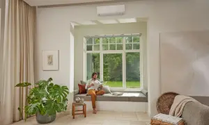 Hombre leyendo en un banco junto a una ventana, con un aire acondicionado instalado arriba. Pregúntate: cuanto se tarda en instalar un aire acondicionado.