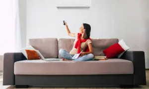 Mujer sentada en sofá, usando control remoto para ajustar uno de los tipos de aire acondicionado.