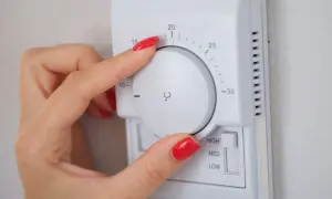 Mano ajustando el termostato para decidir a qué temperatura poner la calefacción en invierno. Se ve el dial con números y la opción de intensidad.