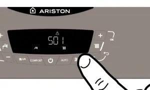 Panel de caldera Ariston con pantalla digital mostrando "501" y un triángulo de advertencia. Un dedo presiona el botón "R" para intentar cómo quitar la luz roja de la caldera.