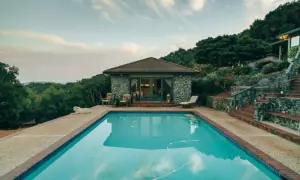 Piscina con agua cristalina, rodeada de vegetación y una casa de piedra. Ideal para climatizar piscina y disfrutar todo el año.