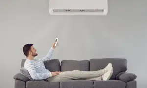 Hombre relajado en sofá, usando control remoto para que el aire acondicionado renueve el aire y refresque la estancia.