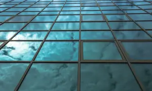 Fachada de edificio con cristales fotovoltaicos reflejando un cielo nublado y azul.