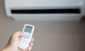 Mano sujetando control remoto de aire acondicionado para combatir el calor. La pantalla muestra 25 grados.