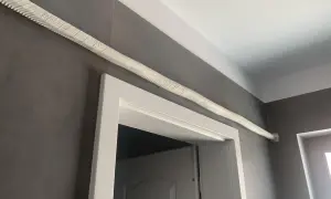 Ideas para tapar tubos aire acondicionado: un tubo blanco texturizado recorre la pared gris sobre un marco de puerta blanco.