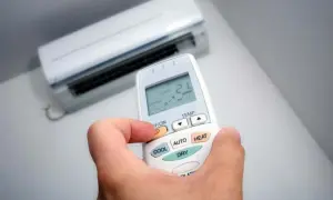 Mano sujetando control remoto de aire acondicionado, ajustando modo deshumidificador.