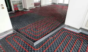 Instalación de sistema de calefacción por suelo radiante, con tuberías rojas sobre paneles negros. La temperatura del suelo radiante se controla desde un colector.