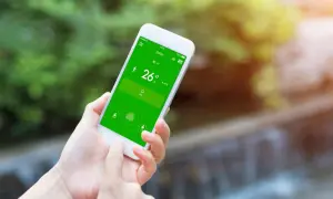 Mano usando un móvil para controlar el aire acondicionado, mostrando la temperatura de 26 grados en la pantalla verde.