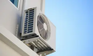 Un aire acondicionado en balcon, montado en la pared blanca de un edificio, con el cielo azul de fondo.