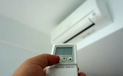 Mano con mando a distancia ajustando el aire acondicionado. Averigua cuanto gasta un aire acondicionado por hora para ahorrar energía.