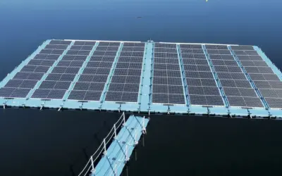Plataforma de energía fotovoltaica flotante sobre un cuerpo de agua azul, con un pasarela azul conectada.