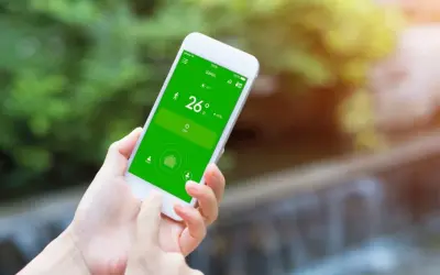Mano usando un móvil para controlar el aire acondicionado, mostrando la temperatura de 26 grados en la pantalla verde.