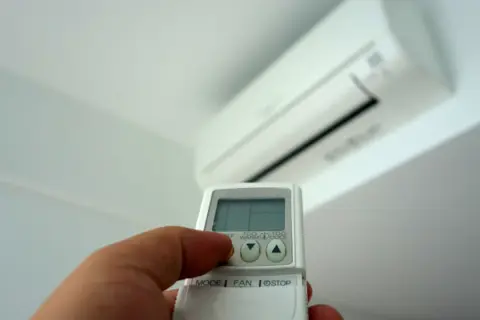 Mano con mando a distancia ajustando el aire acondicionado. Averigua cuanto gasta un aire acondicionado por hora para ahorrar energía.