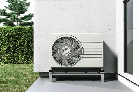 Unidad exterior de aerotermia sin placas solares, instalada junto a una pared blanca y un jardín verde.