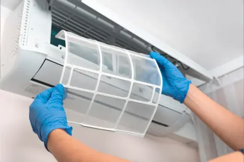 Manos con guantes azules retiran filtro de aire acondicionado. El mantenimiento es clave para saber cuanto dura un aire acondicionado.