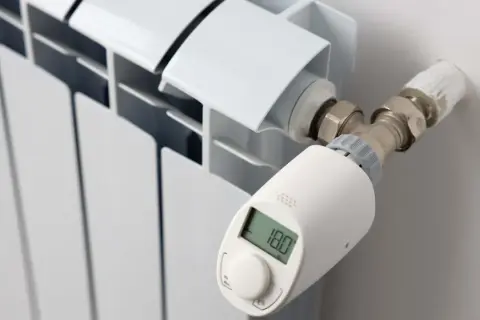 Termostato inteligente en radiador blanco, mostrando 18.0°C. Controla la temperatura en casa para mayor confort.