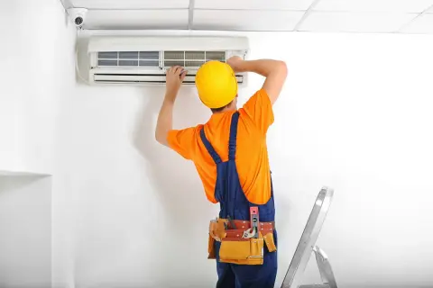 Técnico con casco amarillo instala un aire acondicionado. A pesar de las herramientas, es dificil instalar un aire acondicionado.