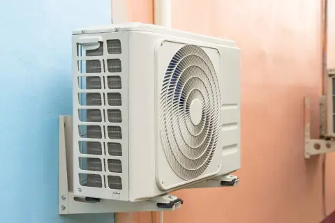 Unidad exterior de aire acondicionado gotea agua. La unidad interior, montada en la pared, muestra su ventilador circular y rejillas de ventilación.