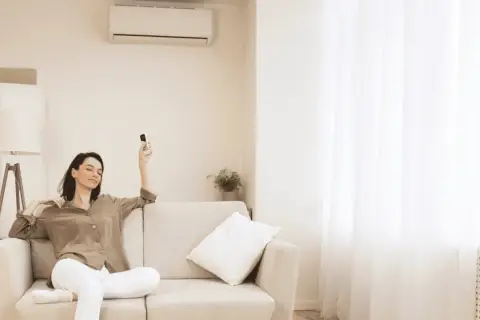 Mujer relajada en sofá con control remoto, pensando cuántas frigorías para 30 metros cuadrados necesita su hogar.