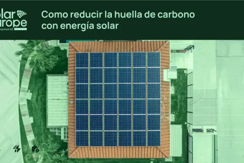 Vista aérea de un tejado con un gran conjunto de placas solares. El texto indica "Cómo reducir la huella de carbono con energía solar".