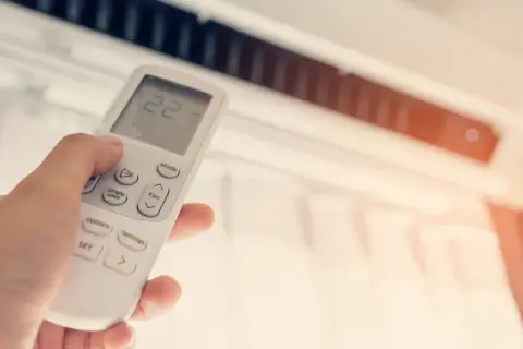 Mano ajustando el control remoto de un aire acondicionado para disfrutar de unas agradables frigorías.