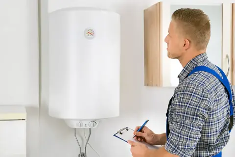 Técnico revisa un termo eléctrico blanco, anotando en una libreta.