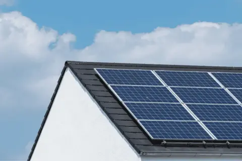 Paneles solares en tejado de casa blanca, bajo un cielo azul con nubes. ¿Cuántas placas solares necesito para una casa?