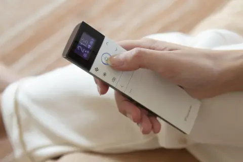 Mano ajustando el control remoto de un cool aire acondicionado a 21 grados.