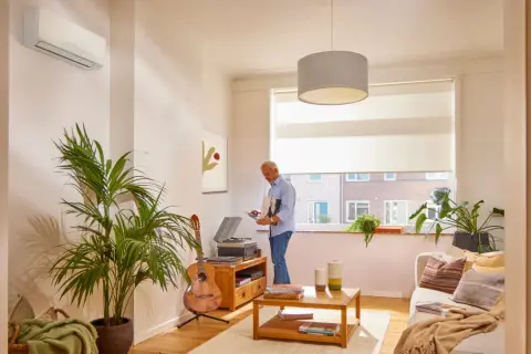 Un hombre elige un disco en un salón acogedor con aerotermia en un piso. Guitarra, plantas y un tocadiscos completan la escena.