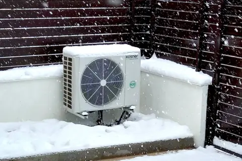 Unidad exterior de bomba de calor Kosner cubierta de nieve, mostrando su capacidad para mantener la temperatura en invierno.