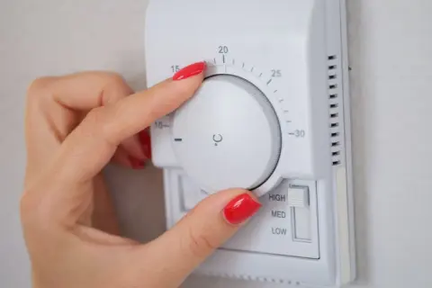 Mano ajustando el termostato para decidir a qué temperatura poner la calefacción en invierno. Se ve el dial con números y la opción de intensidad.