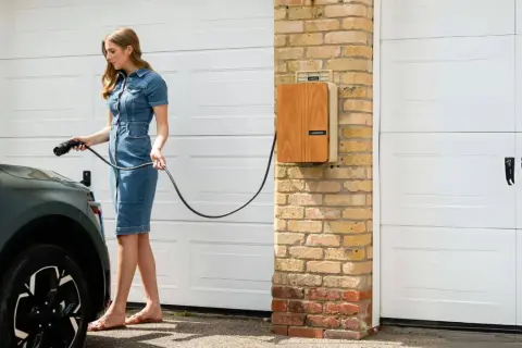 Mujer conecta cargador a coche eléctrico junto a garaje. Solución ideal para instalar punto de recarga en garaje comunitario.