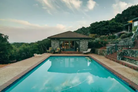 Piscina con agua cristalina, rodeada de vegetación y una casa de piedra. Ideal para climatizar piscina y disfrutar todo el año.