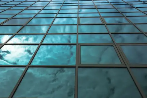 Fachada de edificio con cristales fotovoltaicos reflejando un cielo nublado y azul.