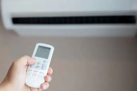 Mano sujetando control remoto de aire acondicionado para combatir el calor. La pantalla muestra 25 grados.