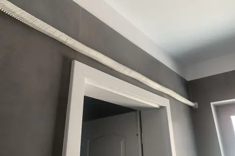 Ideas para tapar tubos aire acondicionado: un tubo blanco texturizado recorre la pared gris sobre un marco de puerta blanco.