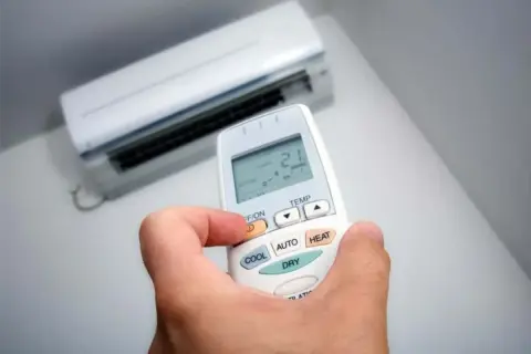 Mano sujetando control remoto de aire acondicionado, ajustando modo deshumidificador.