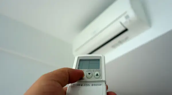 Mano con mando a distancia ajustando el aire acondicionado. Averigua cuanto gasta un aire acondicionado por hora para ahorrar energía.