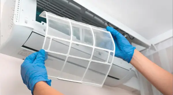 Manos con guantes azules retiran filtro de aire acondicionado. El mantenimiento es clave para saber cuanto dura un aire acondicionado.
