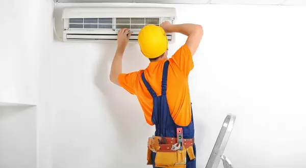 Técnico con casco amarillo instala un aire acondicionado. A pesar de las herramientas, es dificil instalar un aire acondicionado.